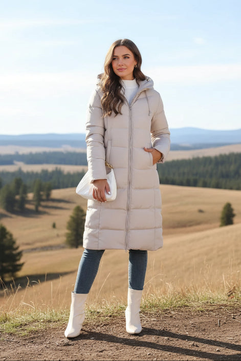 Woman wearing a long beige puffer coat in an urban setting.