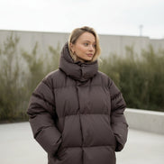 Person wearing a brown puffer jacket in a minimalistic room.