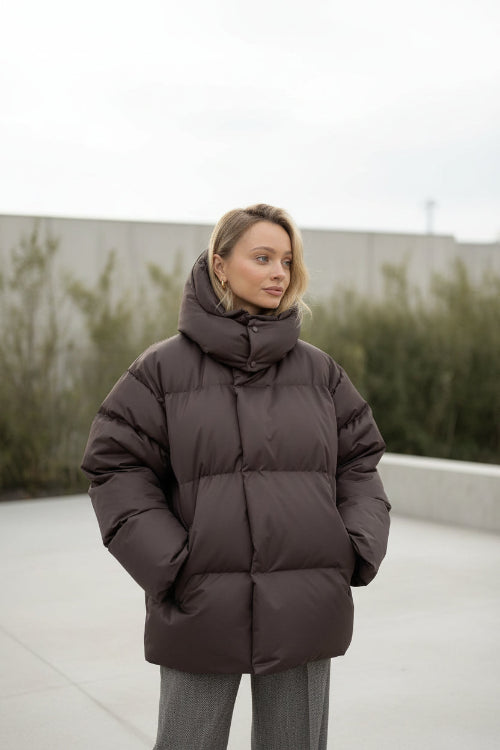 Person wearing a brown puffer jacket in a minimalistic room.