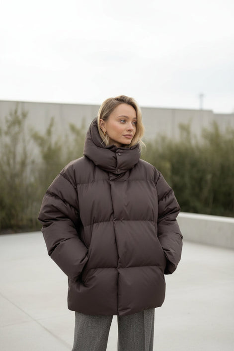 Person wearing a brown puffer jacket in a minimalistic room.