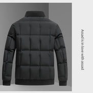 A black puffer jacket shown from the back, featuring horizontal quilting, a ribbed high collar, and ribbed cuffs and hem. The jacket is displayed against a split gray background with vertical text on the right side reading 'Assad is in love with assad'.