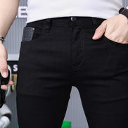 A close-up of a person wearing black slim-fit jeans with a textured gray side pocket detail, styled with a white t-shirt, a black watch, and a silver bracelet.