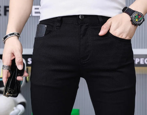 A close-up of a person wearing black slim-fit jeans with a textured gray side pocket detail, styled with a white t-shirt, a black watch, and a silver bracelet.