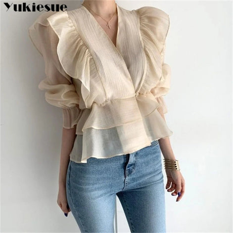 A woman wearing a cream-colored, semi-sheer blouse with dramatic ruffled sleeves and a layered peplum hem, 