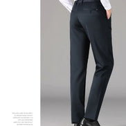 A person shown from the waist down wearing dark charcoal gray slim-fit trousers, a white dress shirt, and black dress shoes against a light gray studio background.