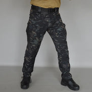 Front view of a model wearing dark camouflage cargo pants with a black belt and black lace-up boots against a gray background.