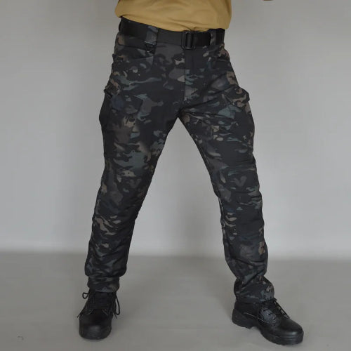 Front view of a model wearing dark camouflage cargo pants with a black belt and black lace-up boots against a gray background.