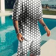 A man wearing a matching black and white geometric patterned t-shirt and shorts set, standing next to a swimming pool.