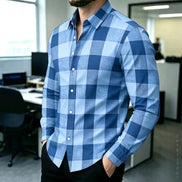 A man wearing a long-sleeve button-up shirt with a blue and light blue buffalo check pattern, standing in an office environment.