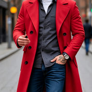 A man wearing a bright red double-breasted overcoat over a dark gray button-up shirt, white t-shirt, and blue jeans, standing on a city street.