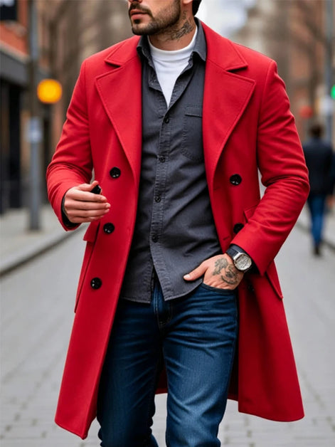 A man wearing a bright red double-breasted overcoat over a dark gray button-up shirt, white t-shirt, and blue jeans, standing on a city street.