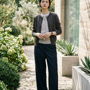 A person sitting on an orange patterned rug in front of a gray textured sofa, wearing a dark gray cardigan over a light gray button-up shirt