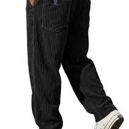 Black pinstriped corduroy pants worn by a model, paired with a white t-shirt and white low-top sneakers, shown from a rear three-quarter angle against a white background.