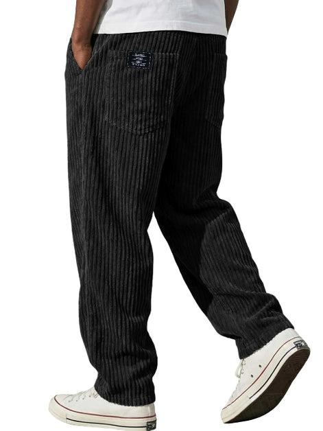 Black pinstriped corduroy pants worn by a model, paired with a white t-shirt and white low-top sneakers, shown from a rear three-quarter angle against a white background.