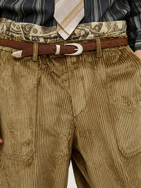 Close-up of a person wearing brown corduroy trousers, a brown belt with a silver buckle, a patterned waistband, a striped shirt, and a striped tie.