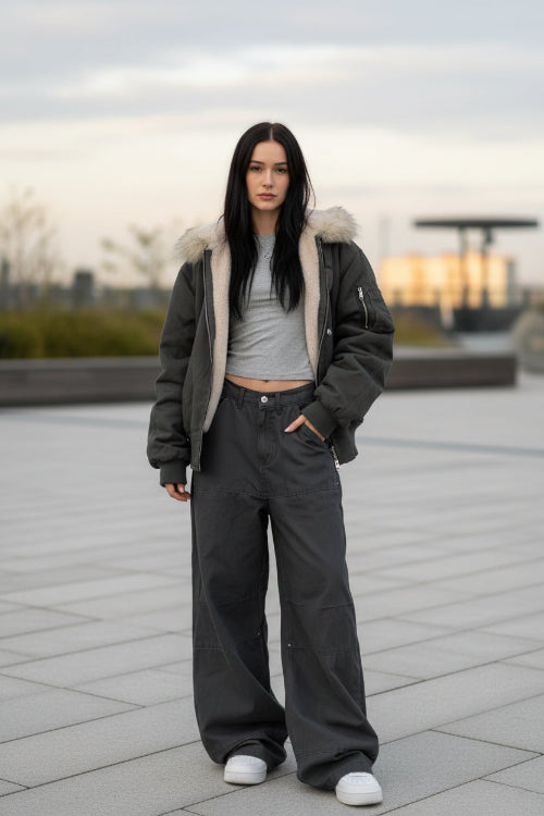 Person wearing a long dark coat with fur trim, standing on a wooden deck.