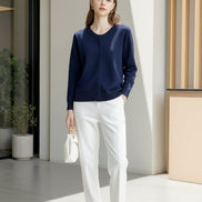 A woman wearing a navy blue long-sleeve button-up knit sweater and white pants, holding a white handbag 