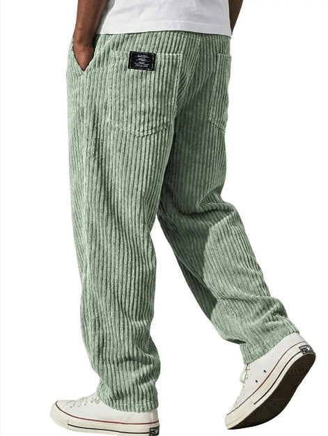 A person wearing green corduroy pants with a white t-shirt and white low-top sneakers, shown from the waist down against a plain white background.