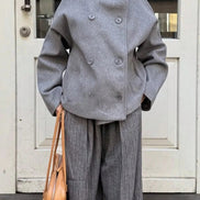 Front view of a woman wearing a gray double-breasted coat with matching pleated trousers