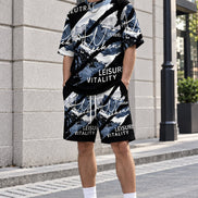 A person wearing a matching black, white, and blue graphic t-shirt and shorts set with white socks and sneakers, standing outdoors against a light-colored stone wall.