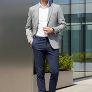 A pair of dark slate blue trousers hanging on a black hanger against a light gray background with a dramatic diagonal shadow.