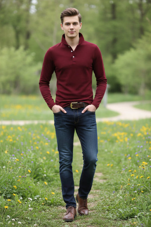 A man wearing a long-sleeve polo shirt in deep burgundy red, paired with dark blue jeans and a brown belt, 