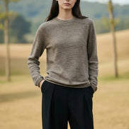 A woman wearing a long-sleeve crewneck knit sweater in a heathered taupe-brown color,