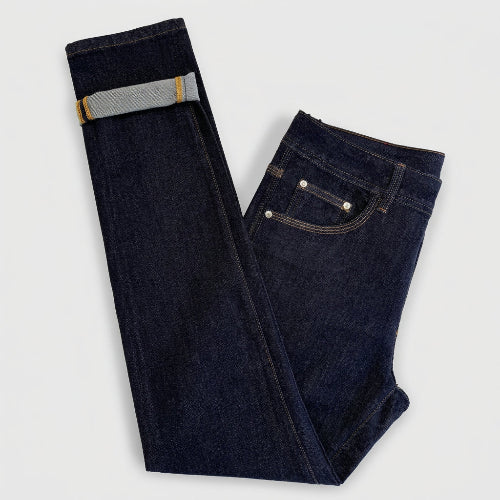 Dark indigo blue jeans folded on a white background, showing the front pocket, belt loop, and rolled cuff revealing a lighter gray inner lining.