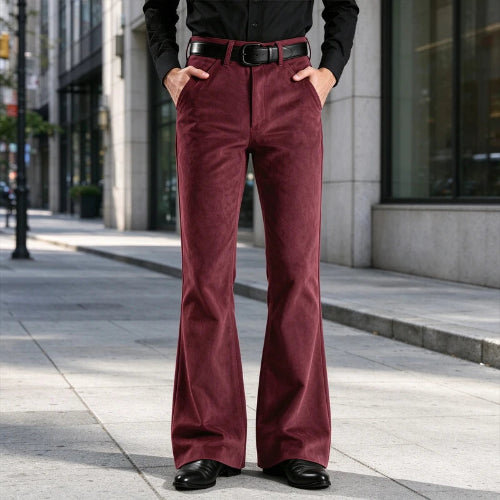 A person standing on a city sidewalk wearing burgundy corduroy flare pants with a black belt, a black long-sleeve shirt, and black shoes.