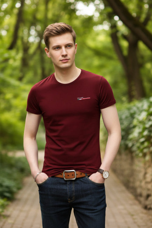 Person wearing a maroon t-shirt with a small logo on a gray background