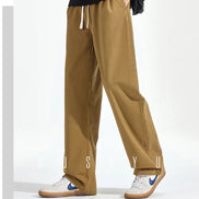 Model wearing khaki loose-fit straight-leg pants with a white drawstring and one hand in a side pocket, paired with white sneakers.