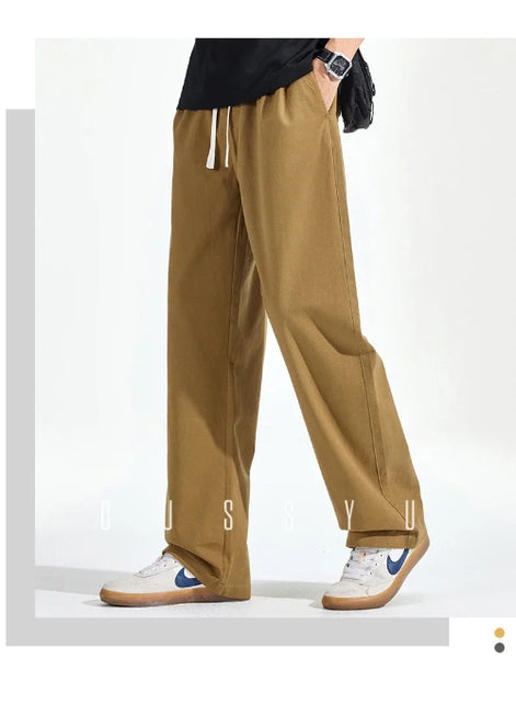 Model wearing khaki loose-fit straight-leg pants with a white drawstring and one hand in a side pocket, paired with white sneakers.