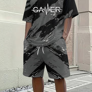 A person wearing a black and gray camouflage-patterned t-shirt and matching shorts with a white 'GAMER' graphic on the chest, 