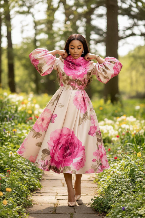 Woman wearing a floral dress with pink flowers holding a gold clutch against a white background