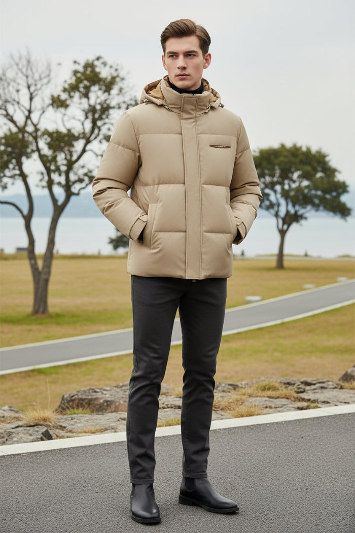 A man wearing a beige hooded puffer jacket with a black turtleneck underneath, shown against a dark gray background with feature callouts on the left.