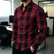 A man wearing a long-sleeve button-up shirt with a red and black buffalo plaid pattern, standing in an office environment.