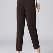 A model wearing dark brown high-waisted ankle-length trousers, paired with a white long-sleeve top and white pointed-toe heels, 