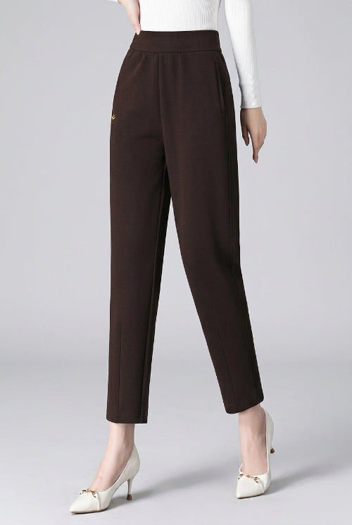 A model wearing dark brown high-waisted ankle-length trousers, paired with a white long-sleeve top and white pointed-toe heels, 