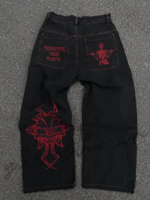 Back view of black wide-leg jeans laid flat, featuring red lettering and a skeleton graphic on the back pockets and a large red cross-style design on one leg.