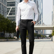 A man wearing slim black dress pants, a white dress shirt, and black dress shoes, holding a black clutch. The Langbeeyar brand logo is visible in the top left corner against a dark gray studio background.