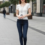 A woman wearing a fitted white short-sleeve V-neck t-shirt with a textured knit pattern, styled with a black and white chain necklace and a hair scrunchie in an outdoor street setting.