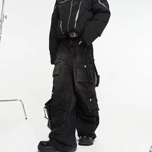 Model wearing washed black baggy cargo jeans with multiple flap pockets and hanging side straps, paired with a black padded jacket and chunky black shoes.