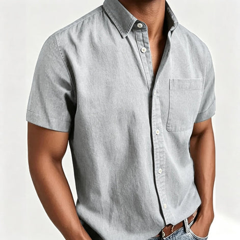 A man wearing a light gray short-sleeve button-up shirt with a chest pocket, paired with blue jeans and a brown belt, shown 