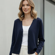 A woman wearing a navy blue knit cardigan sweater with a button-up front, shown from the neck down in a softly lit indoor setting.