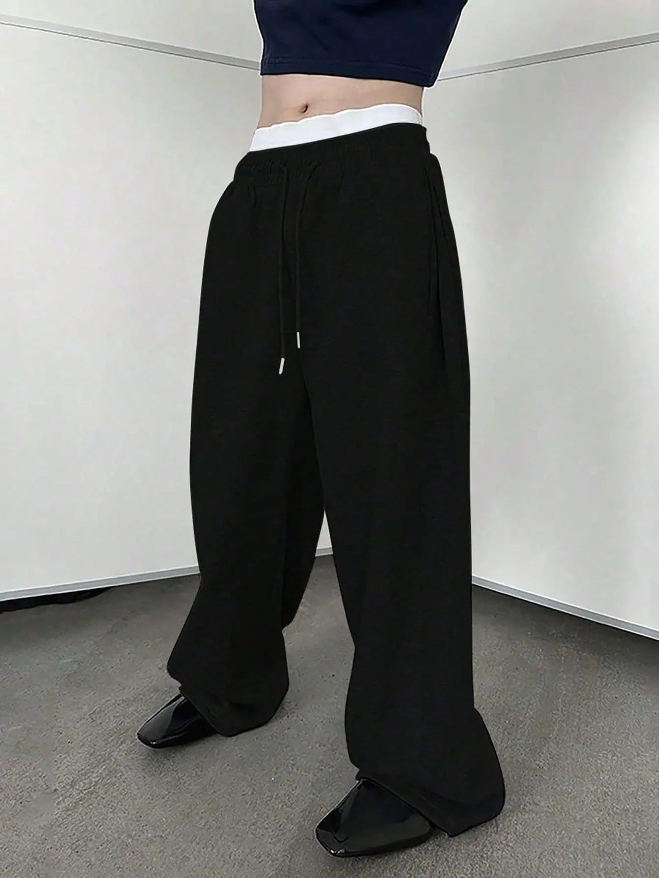 Person wearing black wide-leg pants and a navy top against a white wall.
