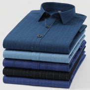 A stack of folded long-sleeve dress shirts in various shades of blue, including navy, light blue, and black, with some shirts featuring subtle vertical pinstripes.