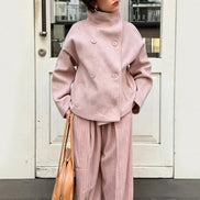 Woman wearing a pale pink double-breasted short coat with matching pleated trousers