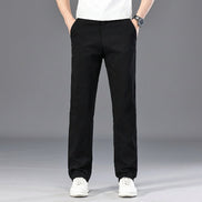 A person wearing black straight-leg pants, a white t-shirt, and white sneakers, standing against a gray studio background. 