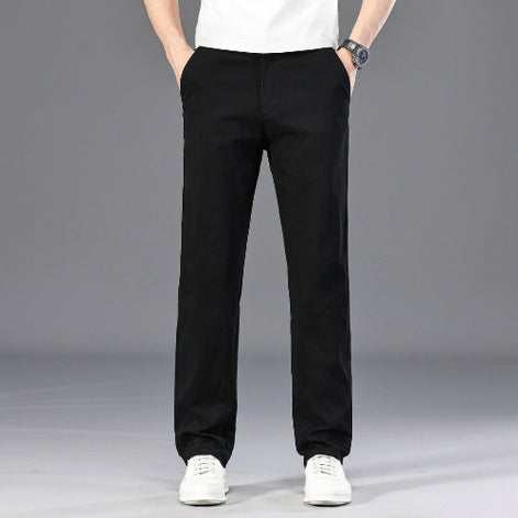 A person wearing black straight-leg pants, a white t-shirt, and white sneakers, standing against a gray studio background. 