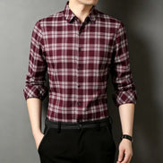 A man wearing a long-sleeve button-up plaid shirt in burgundy and white, paired with black trousers, shown against a dark gray background.